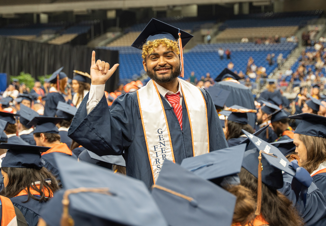 Graduation with a student in cap and grown, standing holding up the 'Birds Up' hand gesture